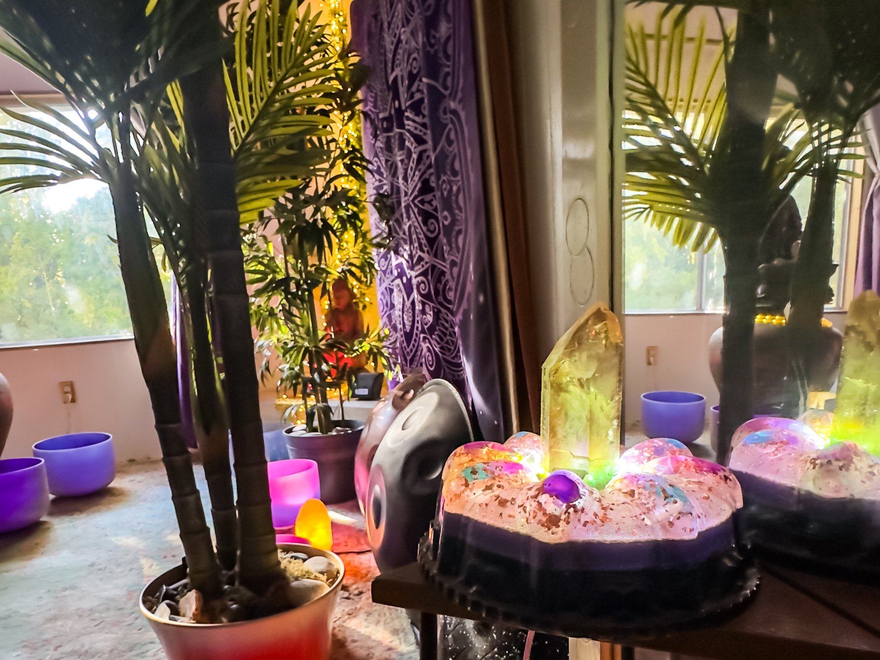 The orgonite generator glowing on its stand in the studio — a citrine point over colored stone spheres, the handpan and crystal bowls behind