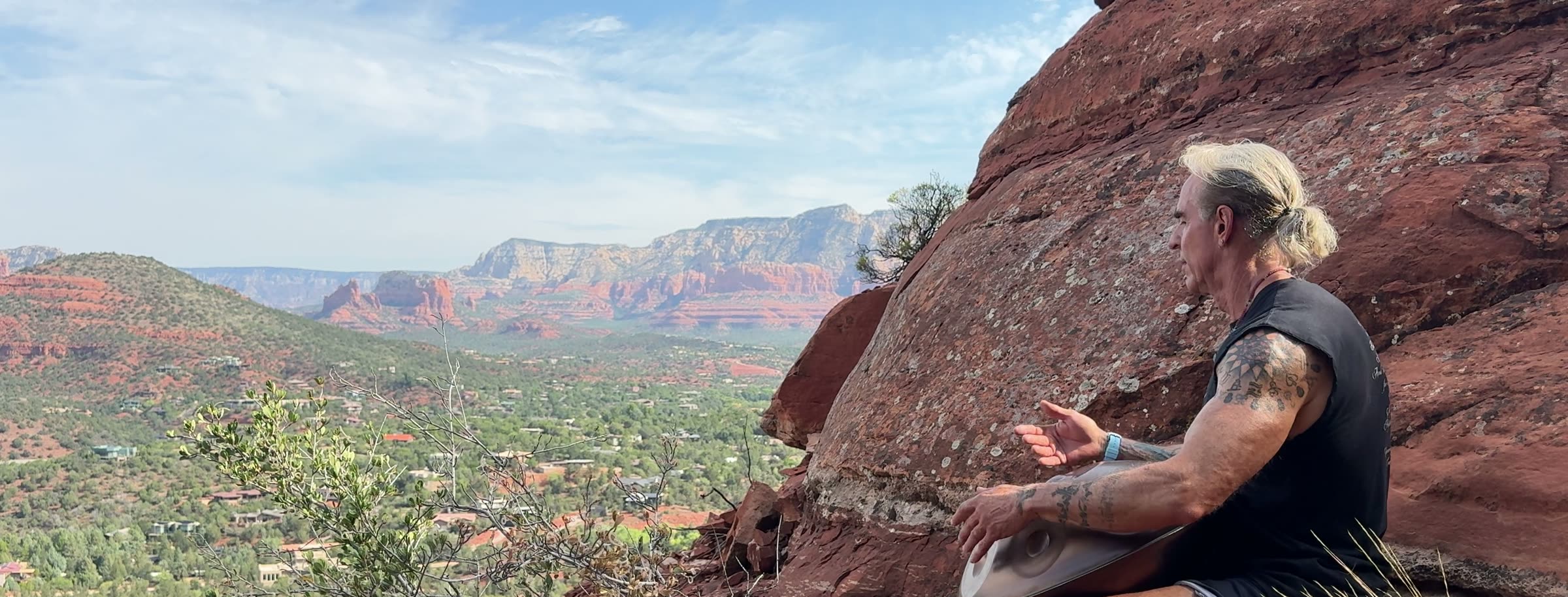 Vance Bleaux playing the handpan on a red-rock ledge high above Sedona, the buttes and the valley behind him